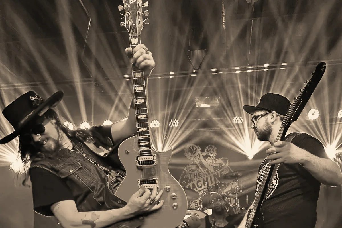 Kidd Lightning with his guitar raised and Alex Blackburn on bass, beams of stage light behind them.