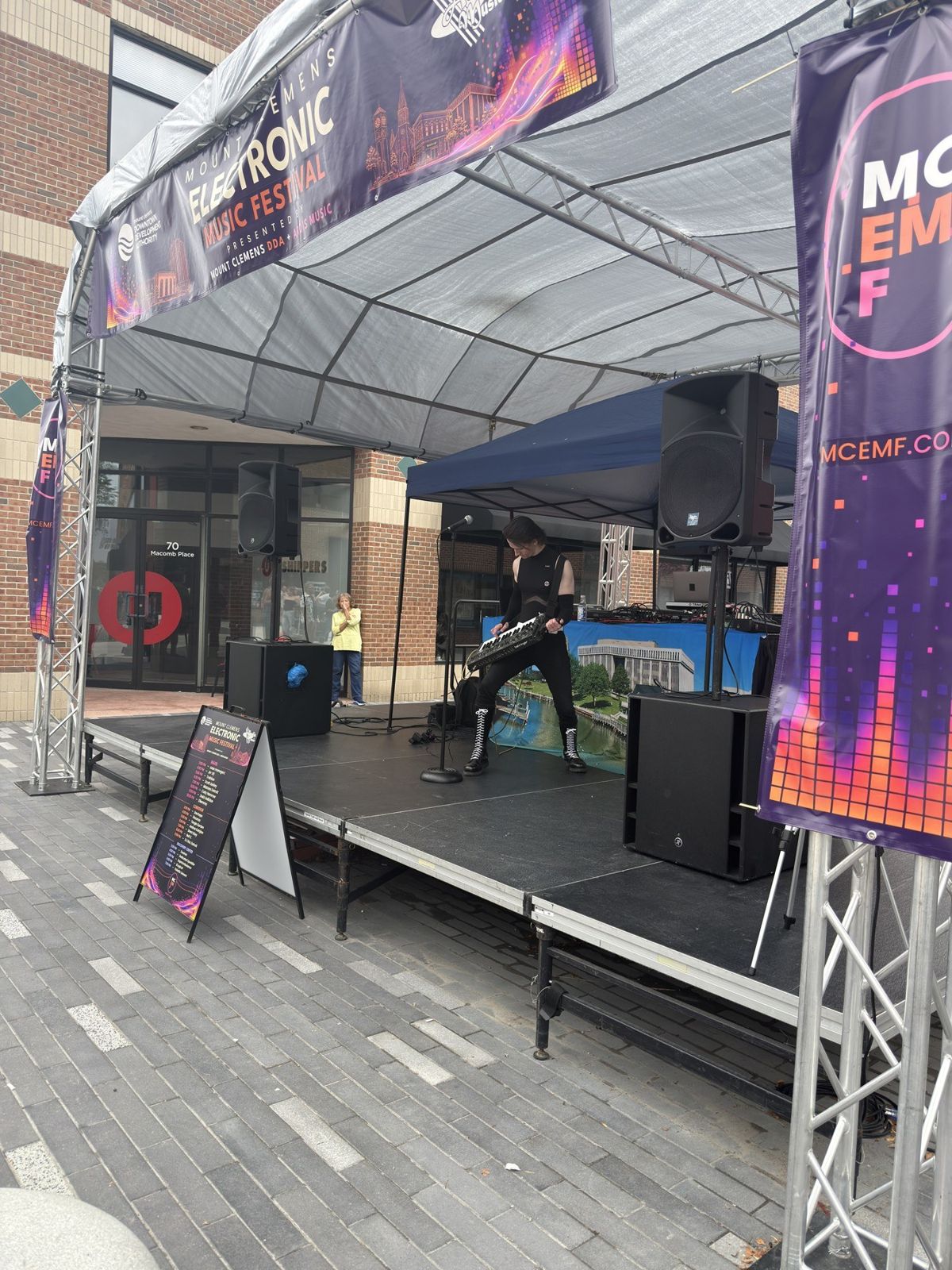 An artist performing on the MCEMF main stage beneath the festival entry arch on Macomb Place.